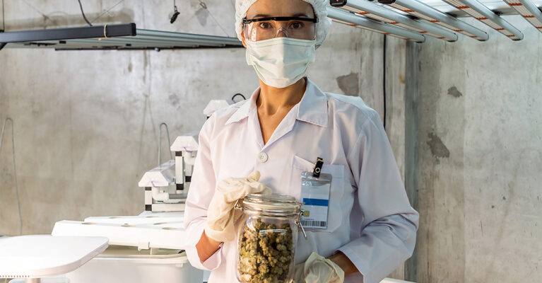 masked doctor holds jar of cannabis flowers