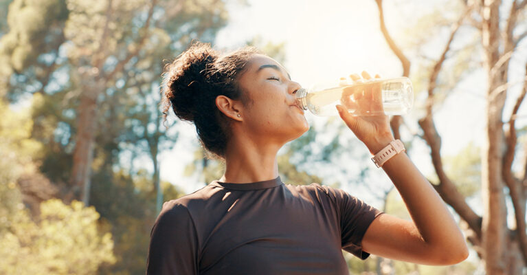 Woman drinking water outdoors, sunlight.