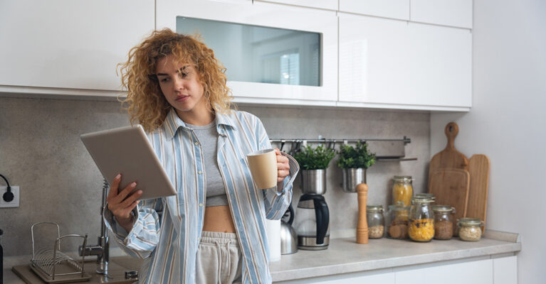 Person in kitchen with tablet and mug